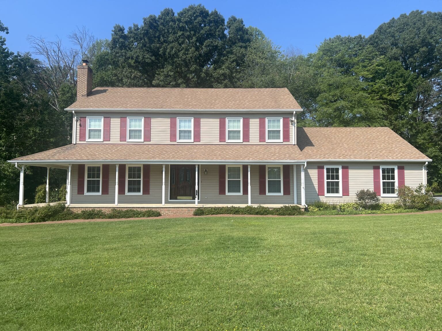 Window and door installation project featuring a two-story home with red shutters and white-trimmed windows.