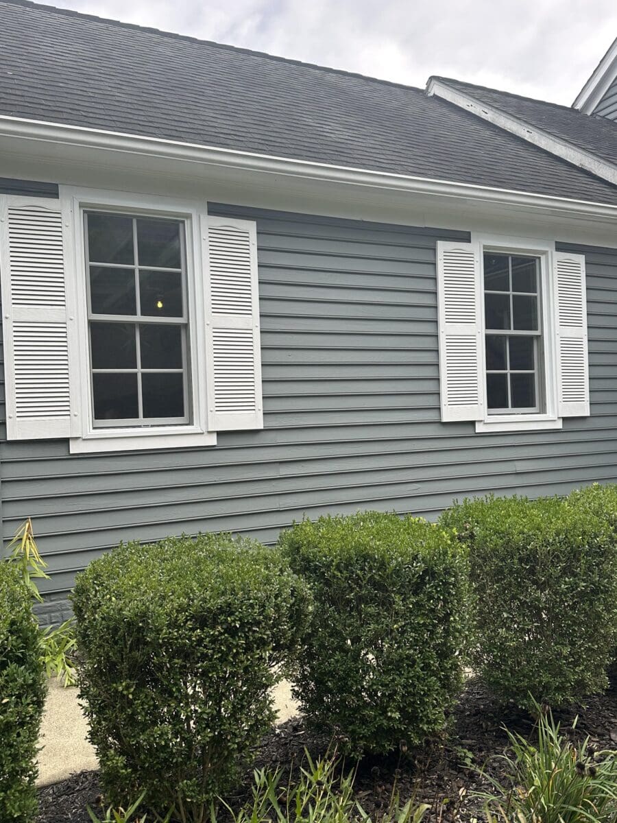 Close-up of gray exterior siding with a white shutter beside a residential window.