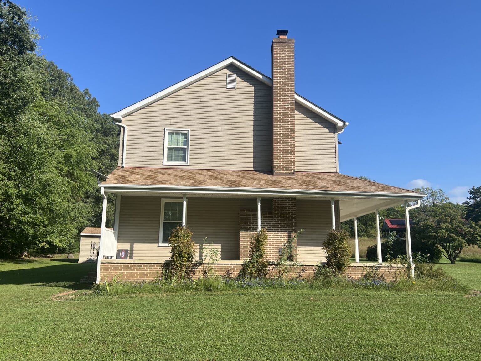 Beige two-story home with white-framed windows, a brick chimney, and a covered front porch.