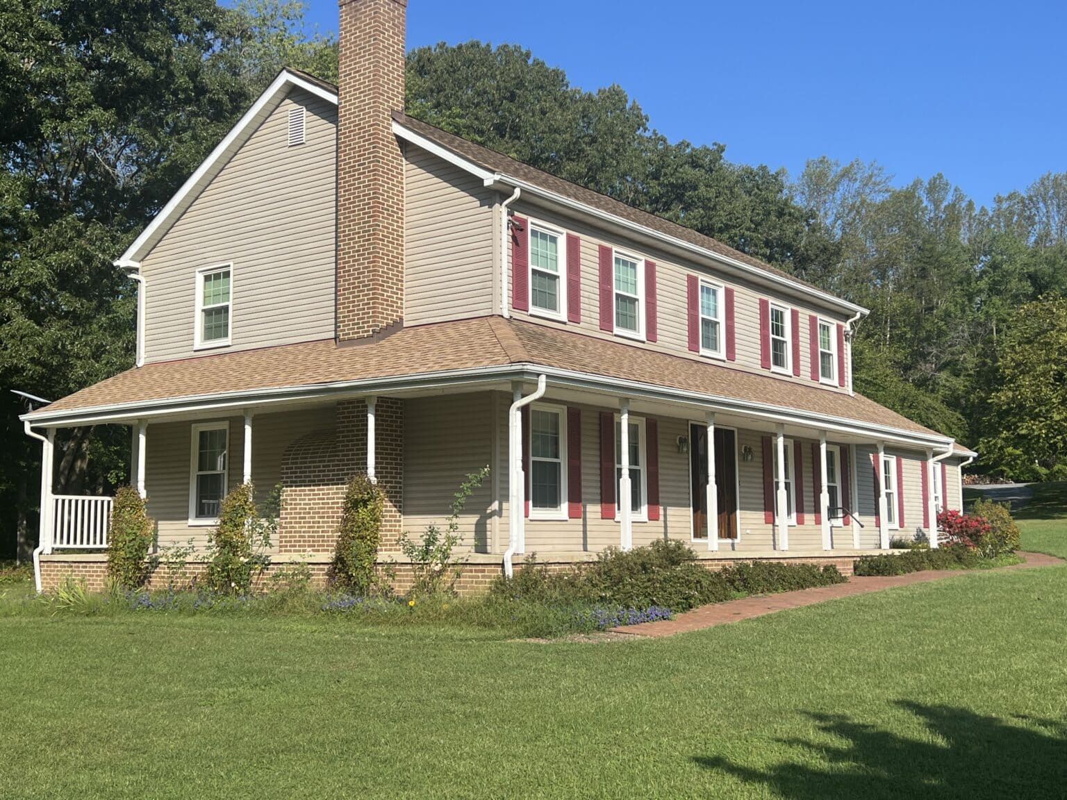 Two-story beige siding home with white-framed windows and red shutters.