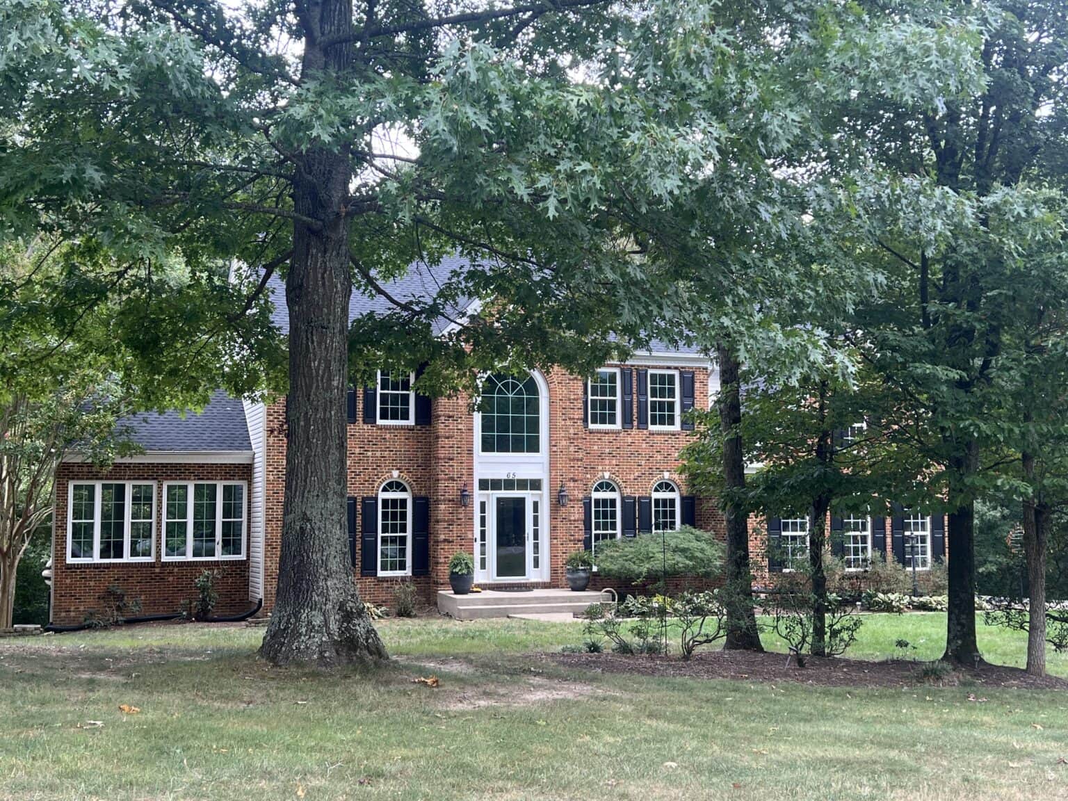 Two-story brick home with white-trimmed windows and mature trees in the front yard.