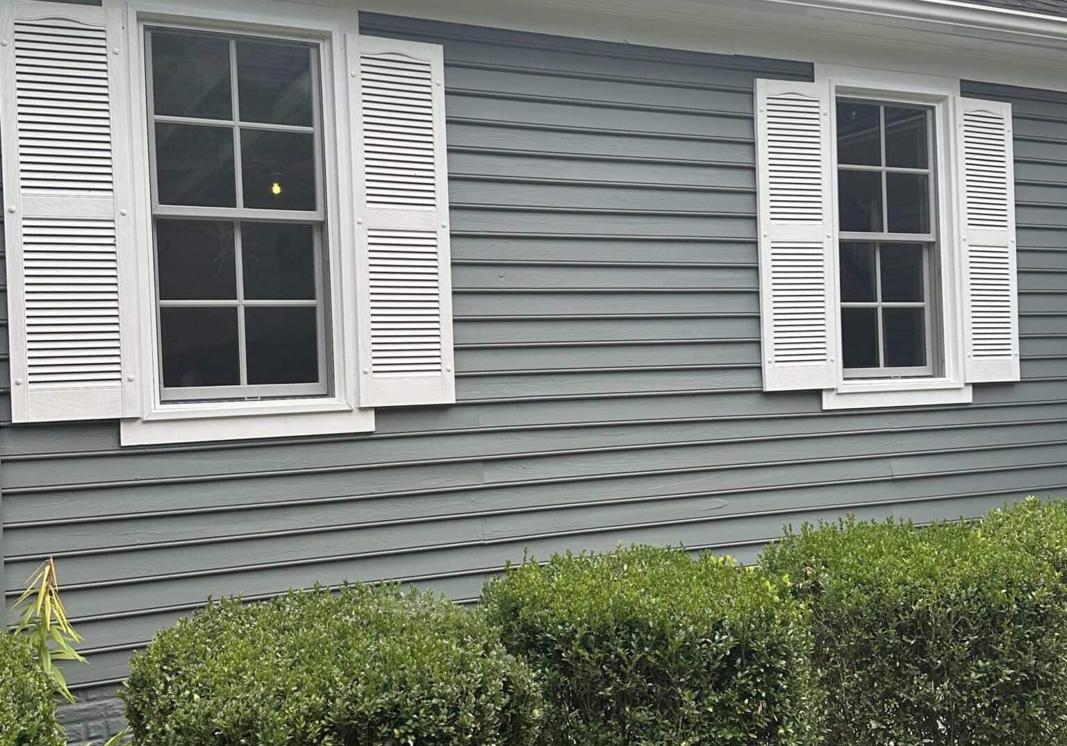 Close-up of gray exterior siding with a white shutter beside a residential window.