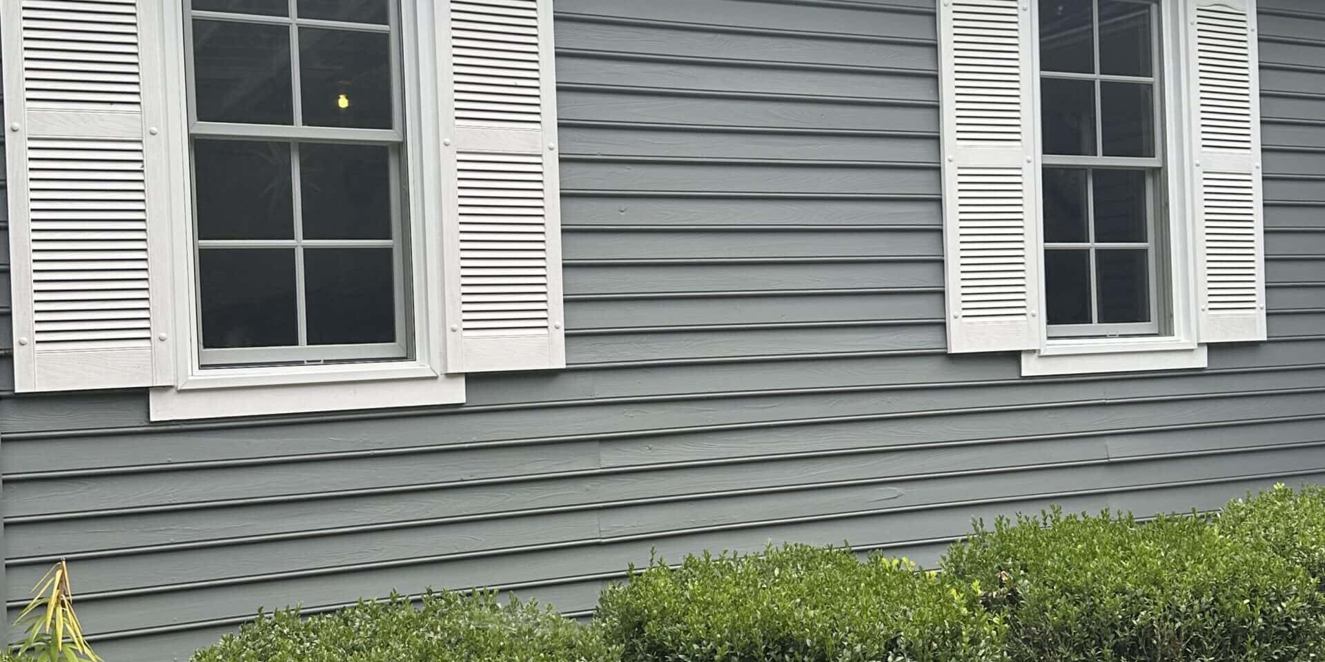 Close-up of gray exterior siding with a white shutter beside a residential window.