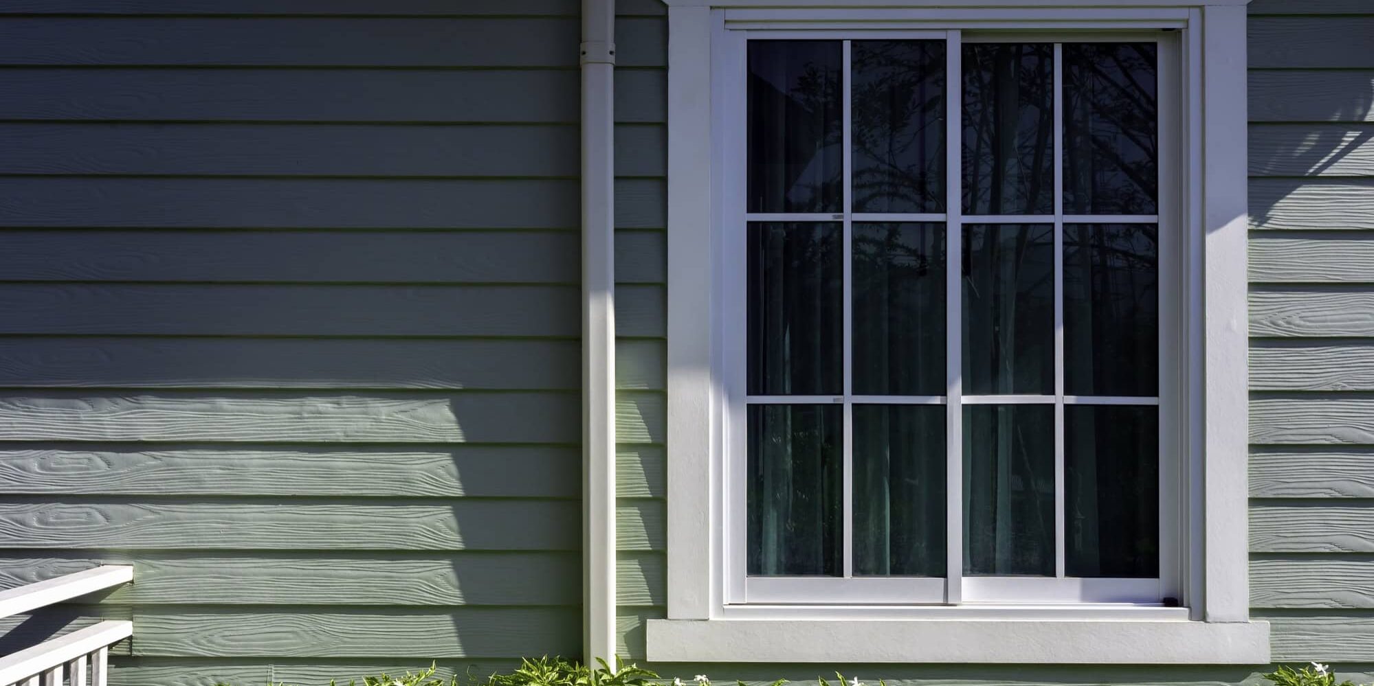 A white house window with glass, green curtain decoration on the small light green wooden resident with copy space, view from outdoor.
