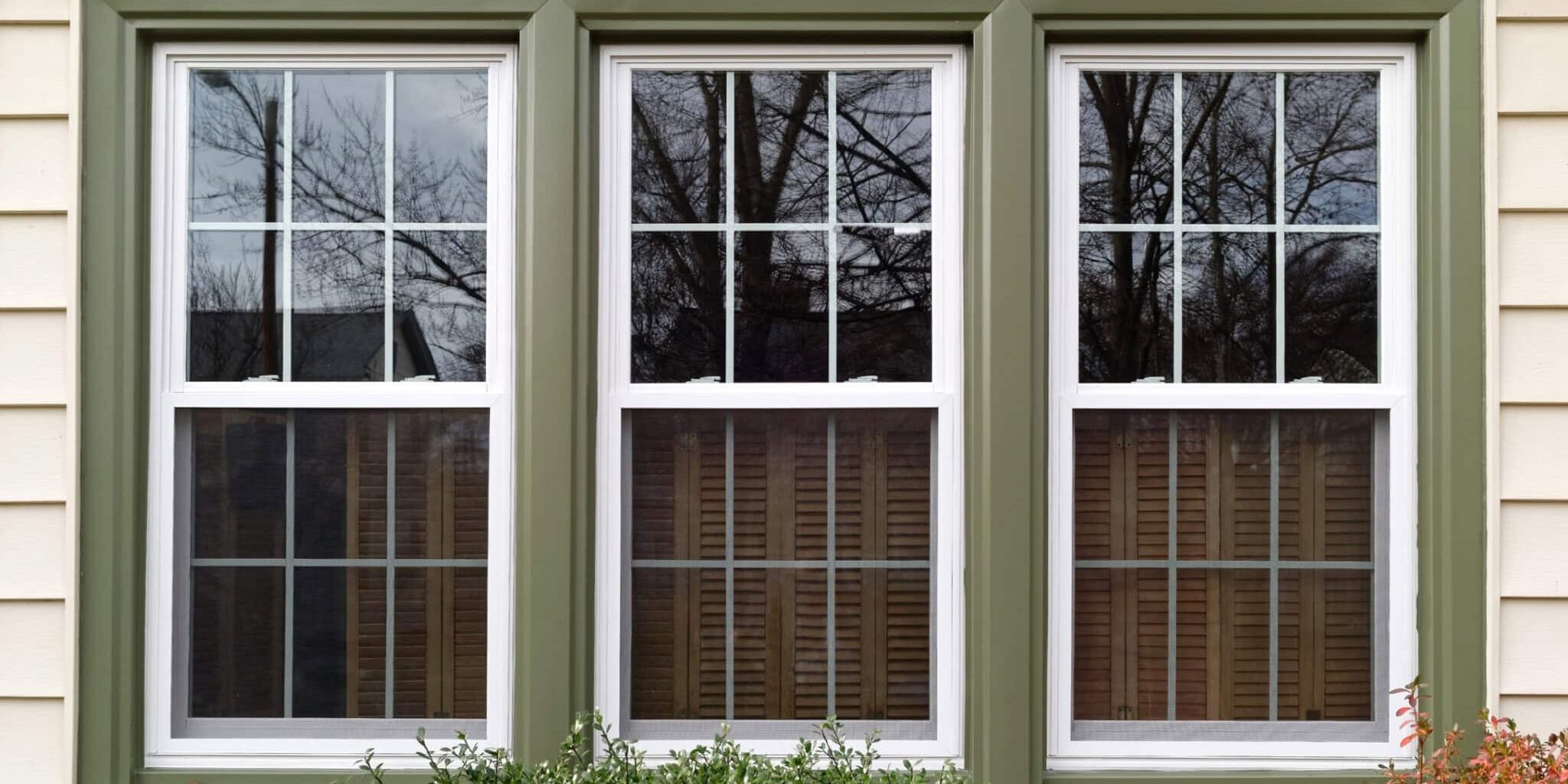 Three new replacement windows with green trim on front of house. Horizontal.
