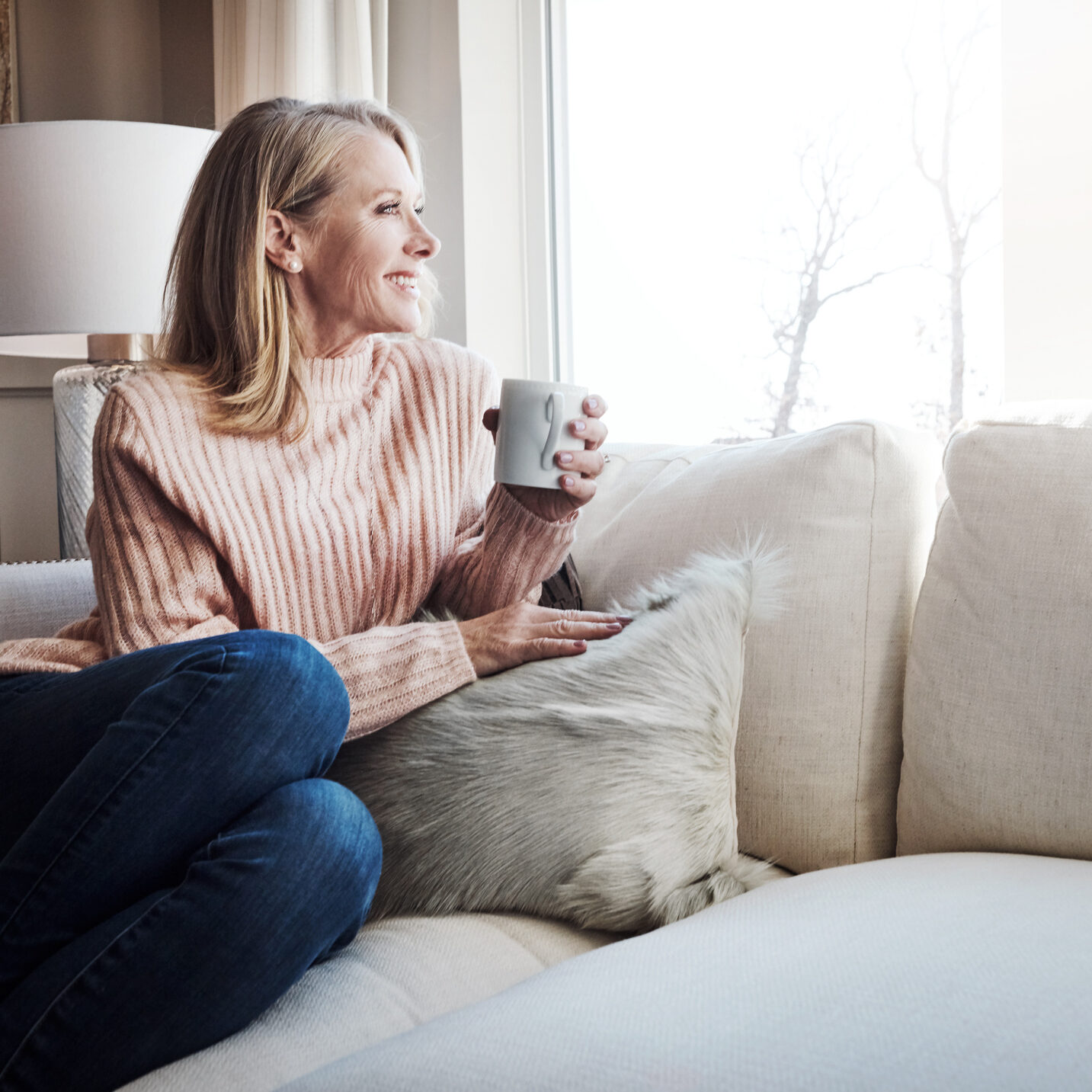 woman relaxing on a sofa beside a bright window in a comfortable living room